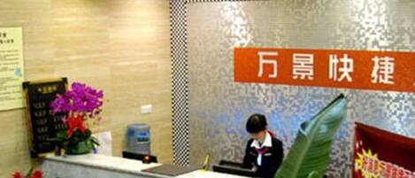 A hotel reception area with a receptionist, a check-in counter, and a decorative wall with a sign.
