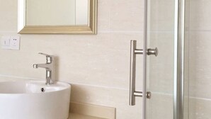 A bathroom with a white sink, a gold-framed mirror, and a glass shower door. - Wanjing Express Hotel (Hangzhou)