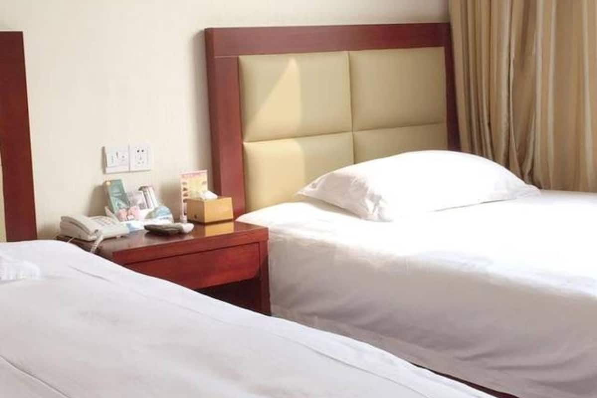 Ein Hotelzimmer mit zwei Betten, einem Holzkopfende, einem Nachttisch mit Telefon und Lampe sowie einem Fenster mit Vorhängen.