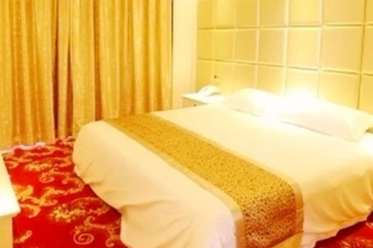 A hotel room with a bed, a nightstand, a lamp, and a window with curtains.