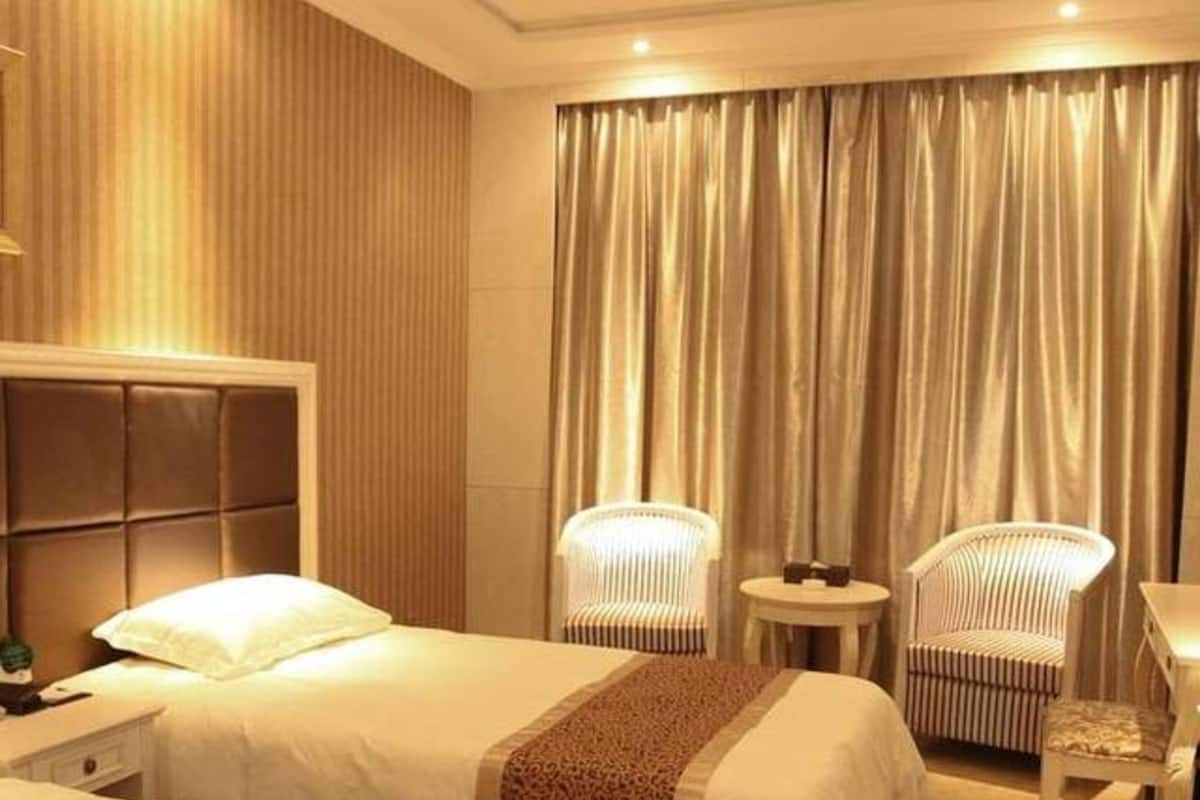 A hotel room with two beds, a small table, two chairs, and a large window with curtains.
