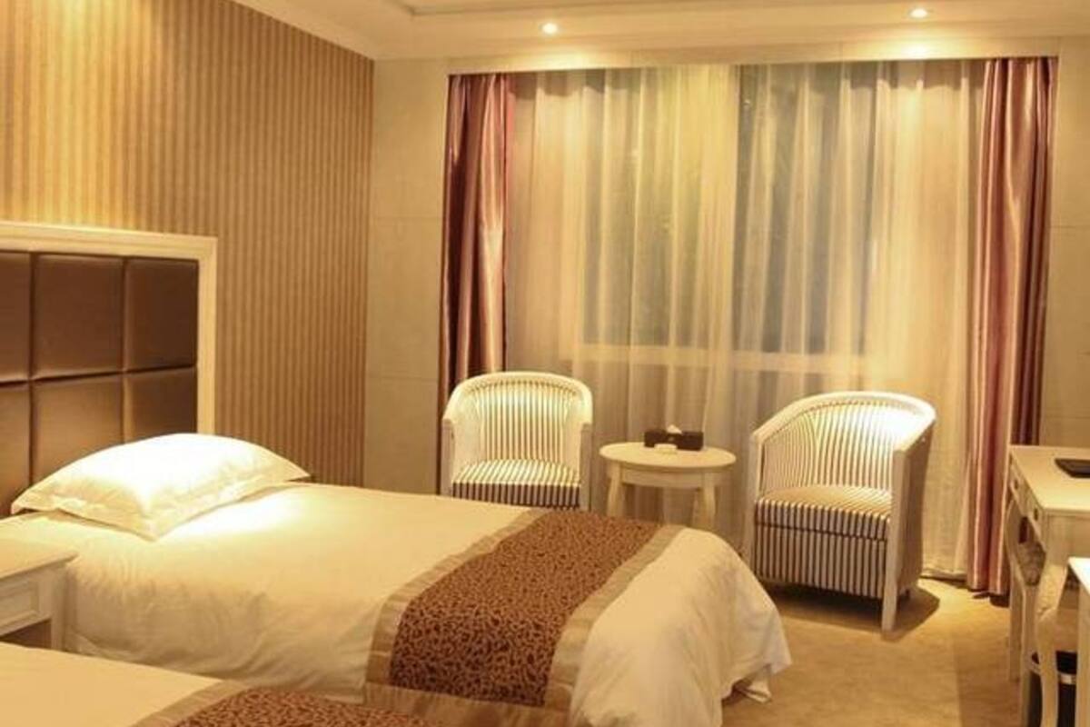 A hotel room with two beds, a small table, two chairs, and a large window with curtains.