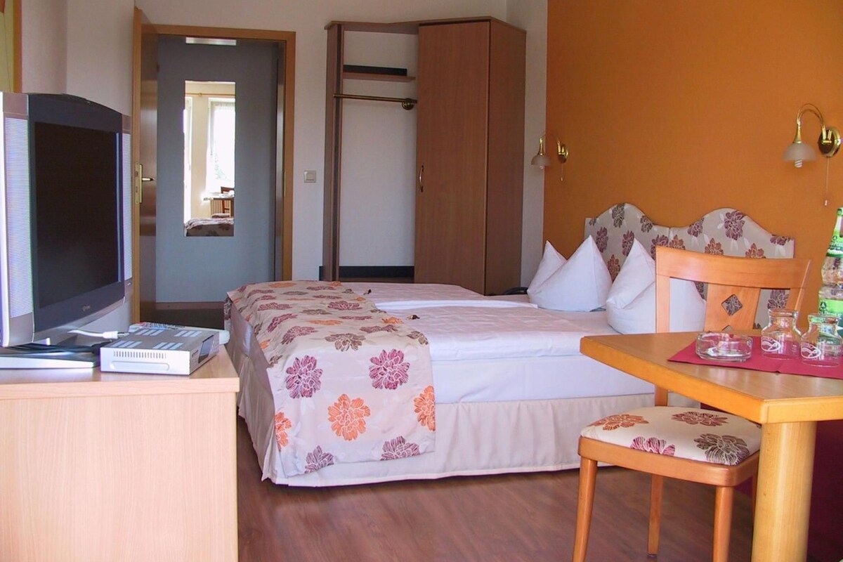 A hotel room with a bed, a desk with a computer, a television, and a wardrobe.