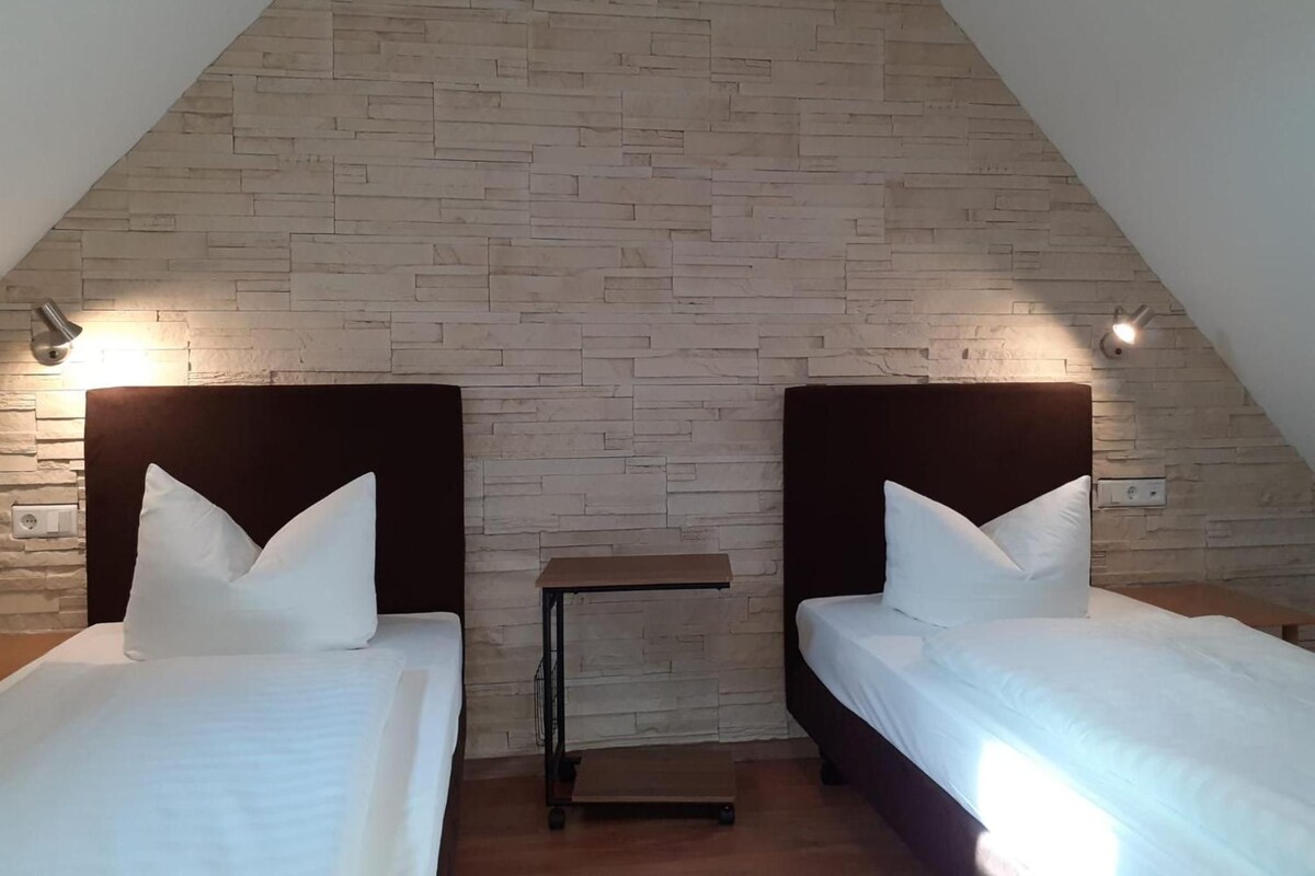 A room with two beds, a small table, and a sloped ceiling.
