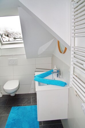 A modern bathroom with a skylight, white fixtures, a toilet, and a blue towel. - Haus Auszeit (Rauris)