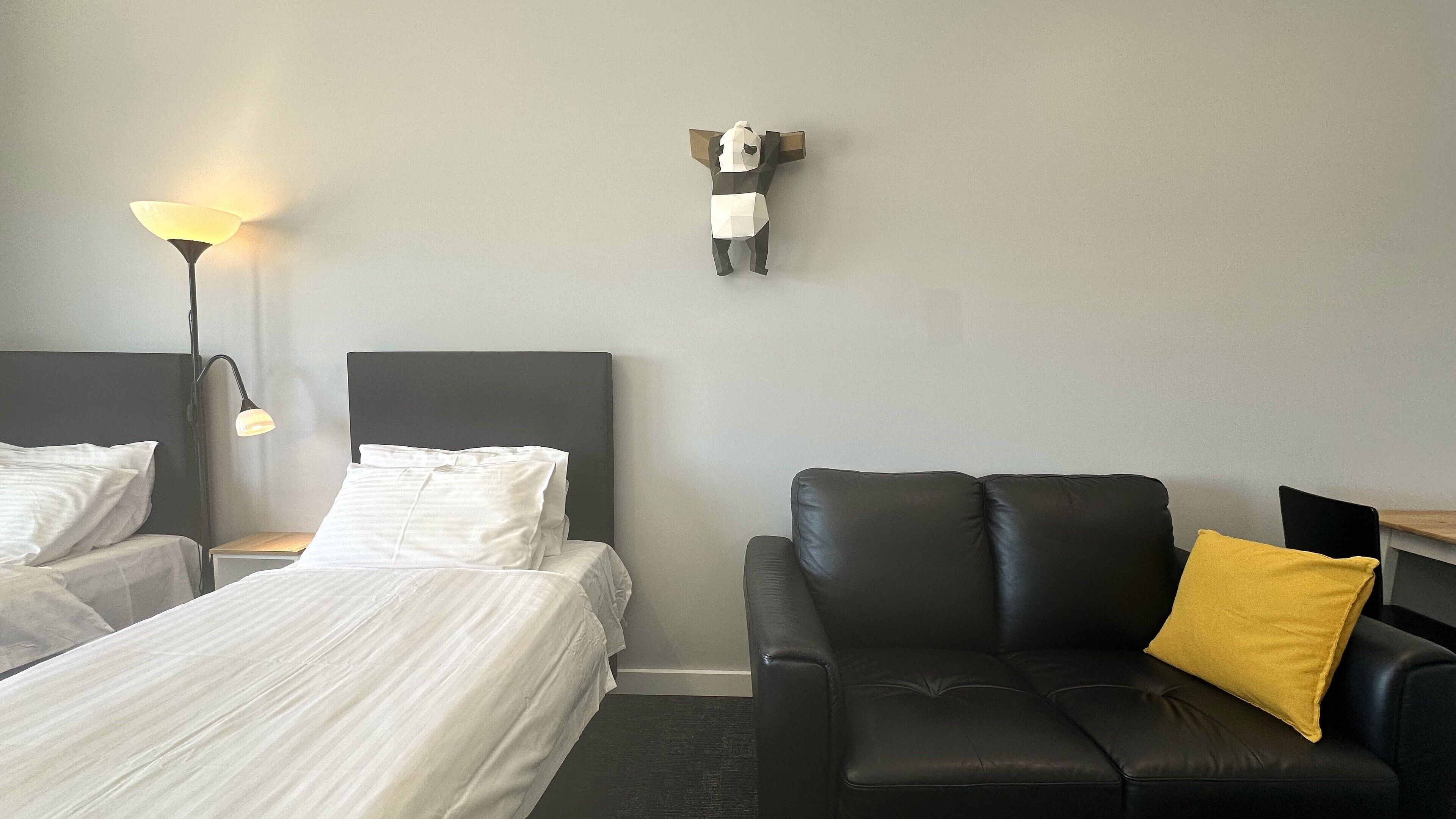 Ein Hotelzimmer mit zwei Betten, einem schwarzen Ledersofa mit gelbem Kissen und einer Wanddekoration.