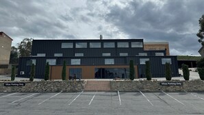 Un edificio moderno con techo plano, ventanas amplias y una pared de piedra con una escalera que lleva a la entrada.