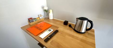 A kitchen counter with a kettle, a digital scale, a knife block, and a small vase with a flower.