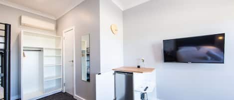Ein Hotelzimmer mit integriertem Schreibtisch, einem an der Wand montierten Fernseher, einem Kleiderschrank und einem Spiegel.
