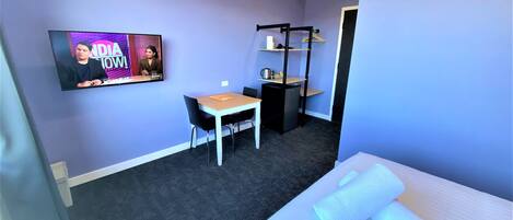 Een hotelkamer met een bed, een bureau, een stoel, een aan de muur bevestigde televisie en een klein kitchenette.