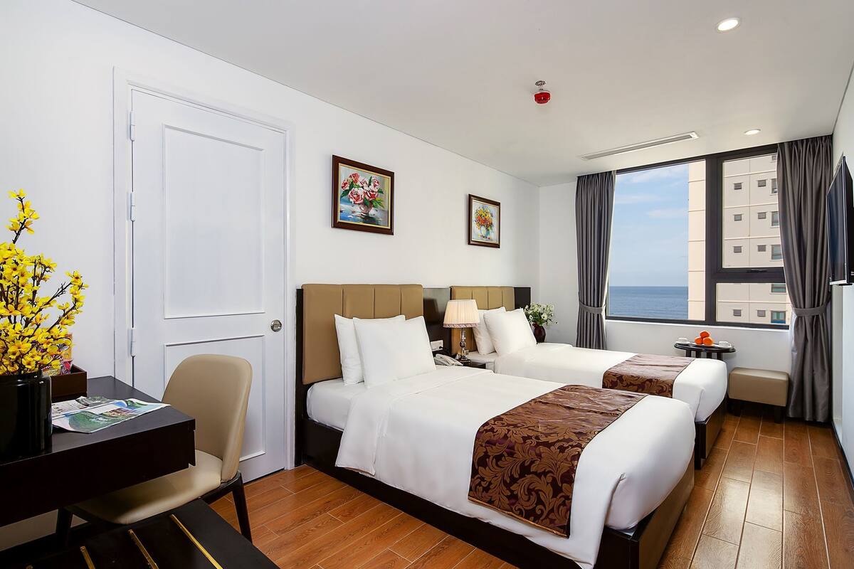 Habitación de hotel con dos camas, un escritorio, una silla, una mesita y una ventana con cortinas.