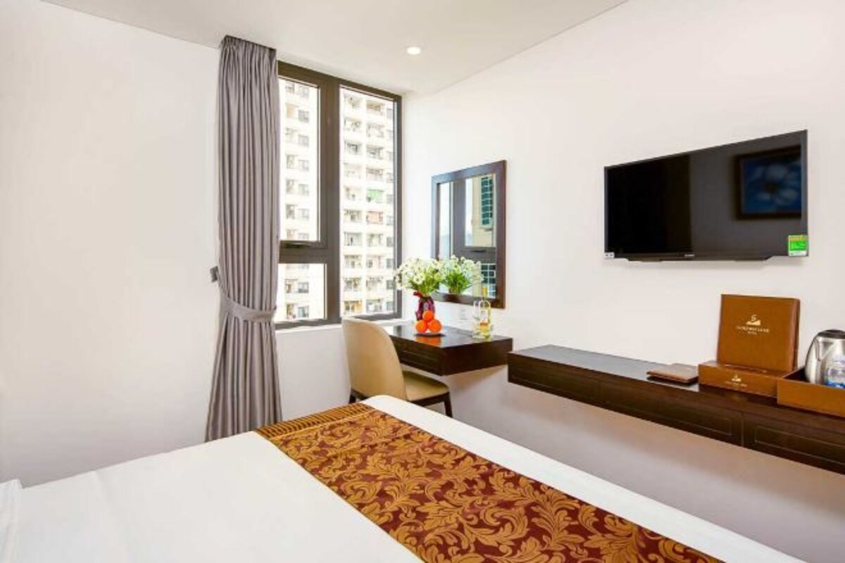 A hotel room with a bed, a desk, a chair, a TV, and a window with curtains.