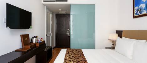 A hotel room with a bed, a TV, a desk with a coffee maker, and a painting on the wall.