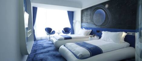 A modern hotel room with two beds, a large window with curtains, a wall mural, and a blue carpet.