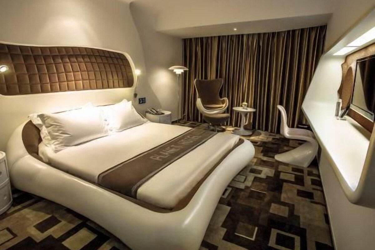 A modern hotel room with a large bed, a seating area with a chair and a small table, and a television.