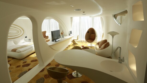 Quarto moderno e com design diferenciado, com uma banheira branca curva, espelho redondo e uma janela grande com cortinas.