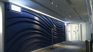 Um corredor moderno com parede azul texturizada, uma placa de metal, uma lixeira e uma seta indicativa no chão.