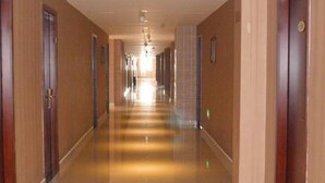 Un pasillo largo y bien iluminado con puertas de madera a ambos lados, que conduce a un final luminoso.