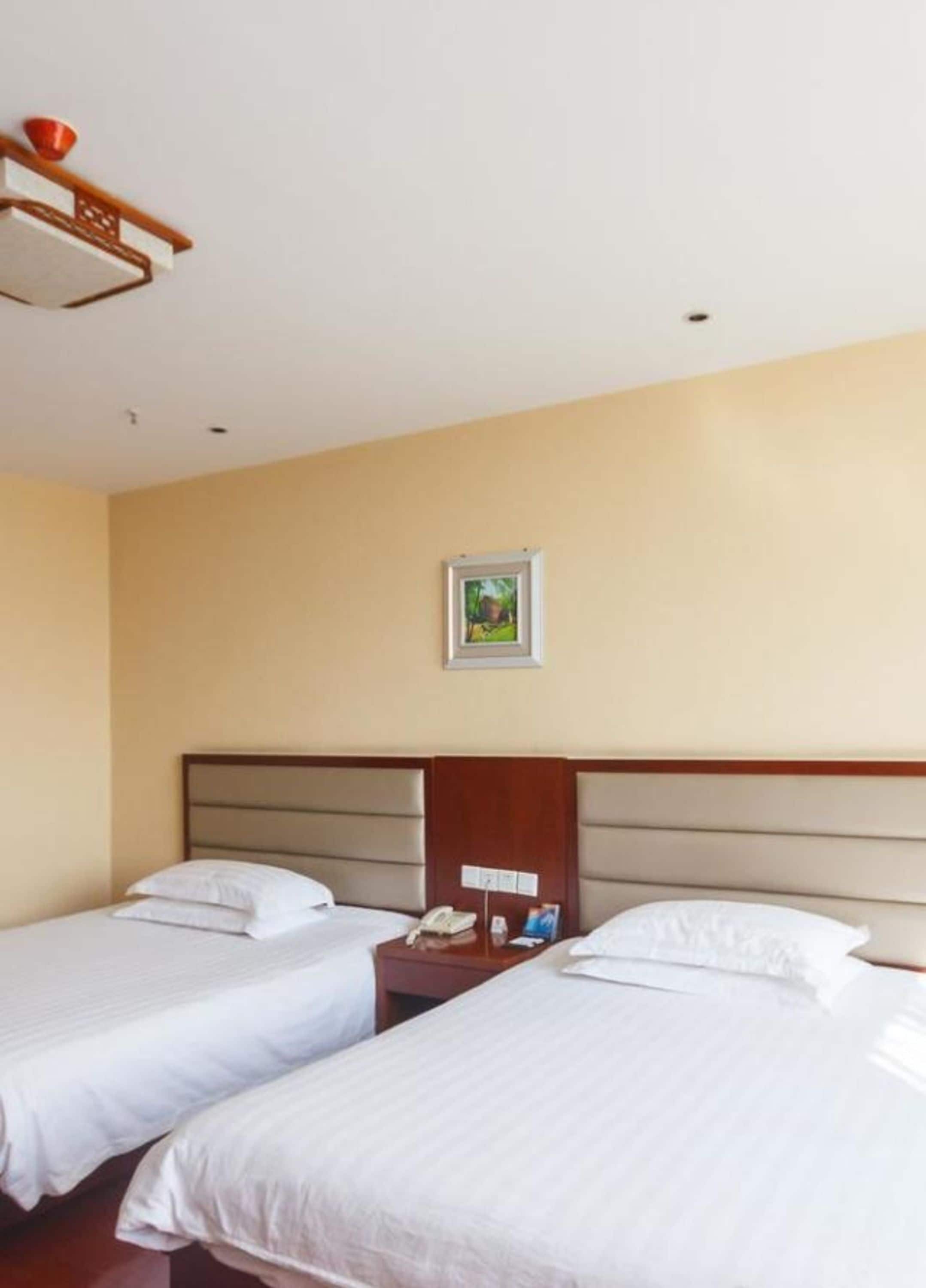 A hotel room with two single beds, a wooden headboard, a nightstand with a phone, and a framed picture on the wall.