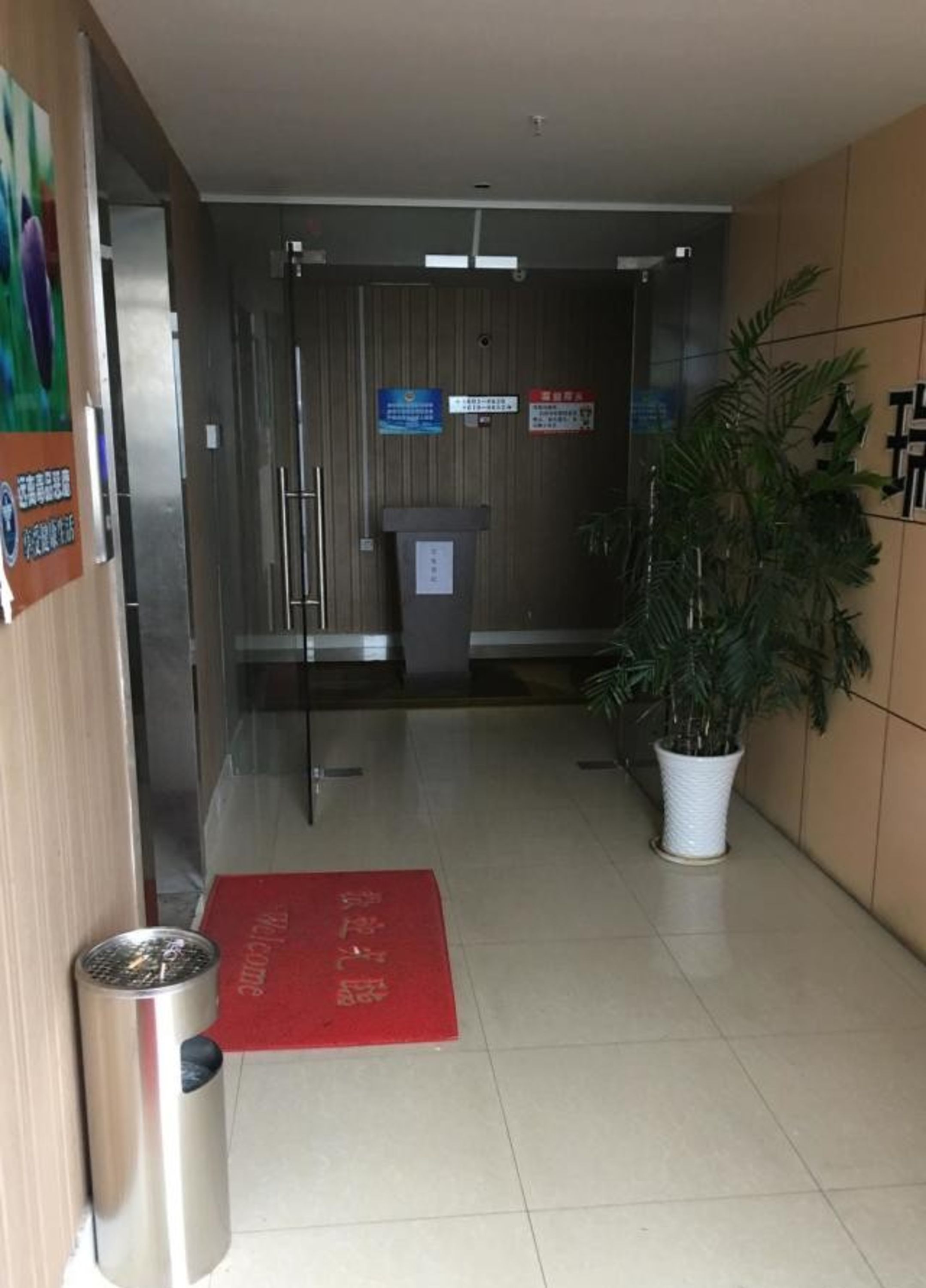 A hotel lobby with a reception desk, a trash bin, a red mat, and a potted plant.