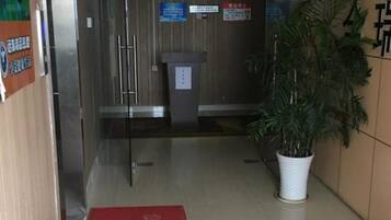 A hotel lobby with a reception desk, a trash bin, a red mat, and a potted plant.