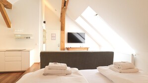 Una habitación de hotel moderna con techo inclinado, un televisor de pantalla plana en la pared y dos camas con toallas ordenadas.