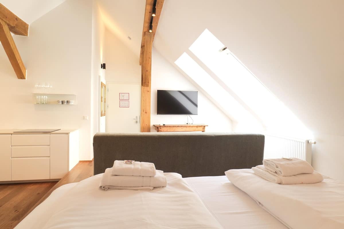 Una habitación de hotel moderna con techo inclinado, un televisor de pantalla plana en la pared y dos camas con toallas ordenadas.