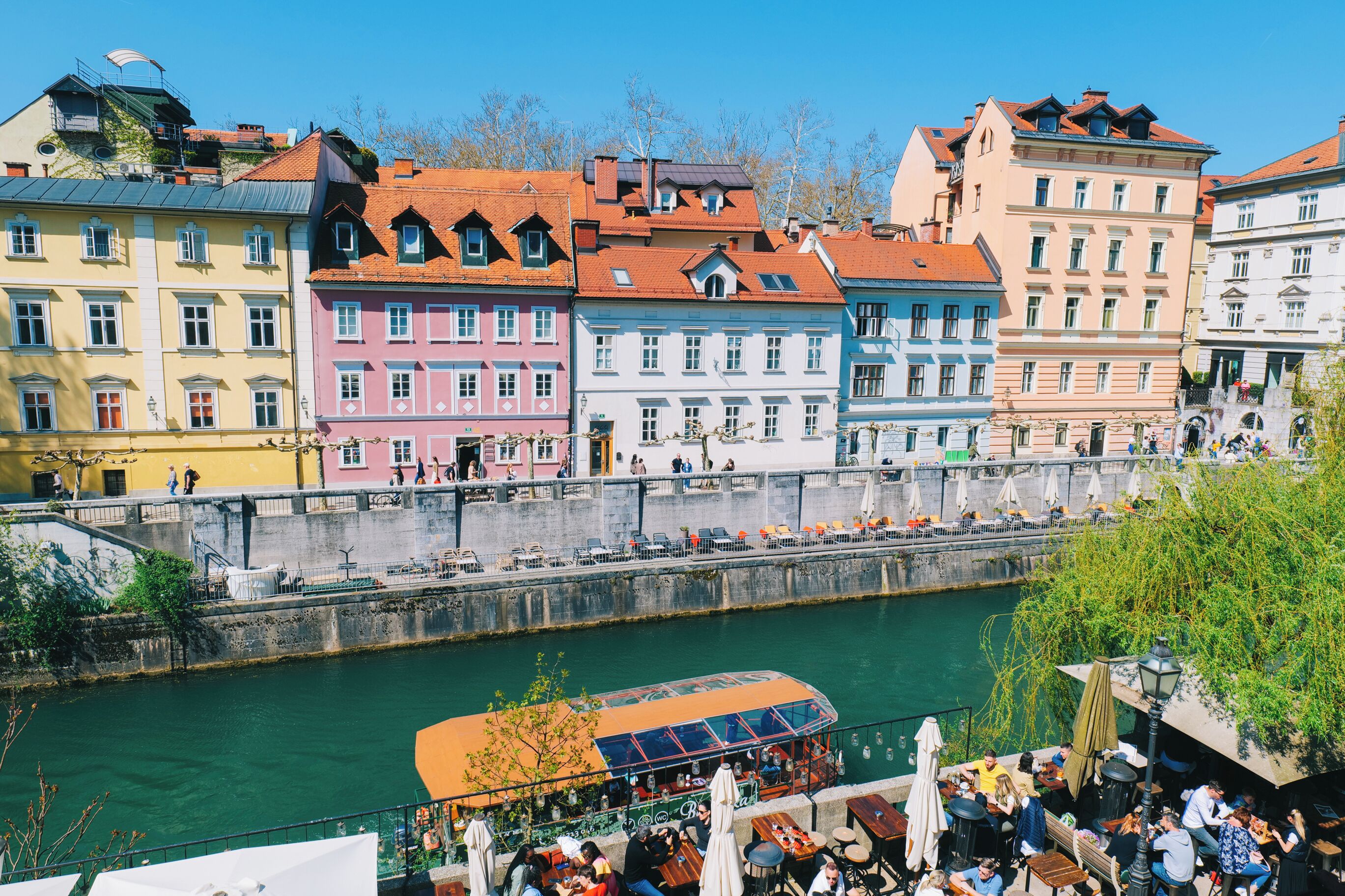 A riverside view of colorful buildings with outdoor seating areas and a boat dock.