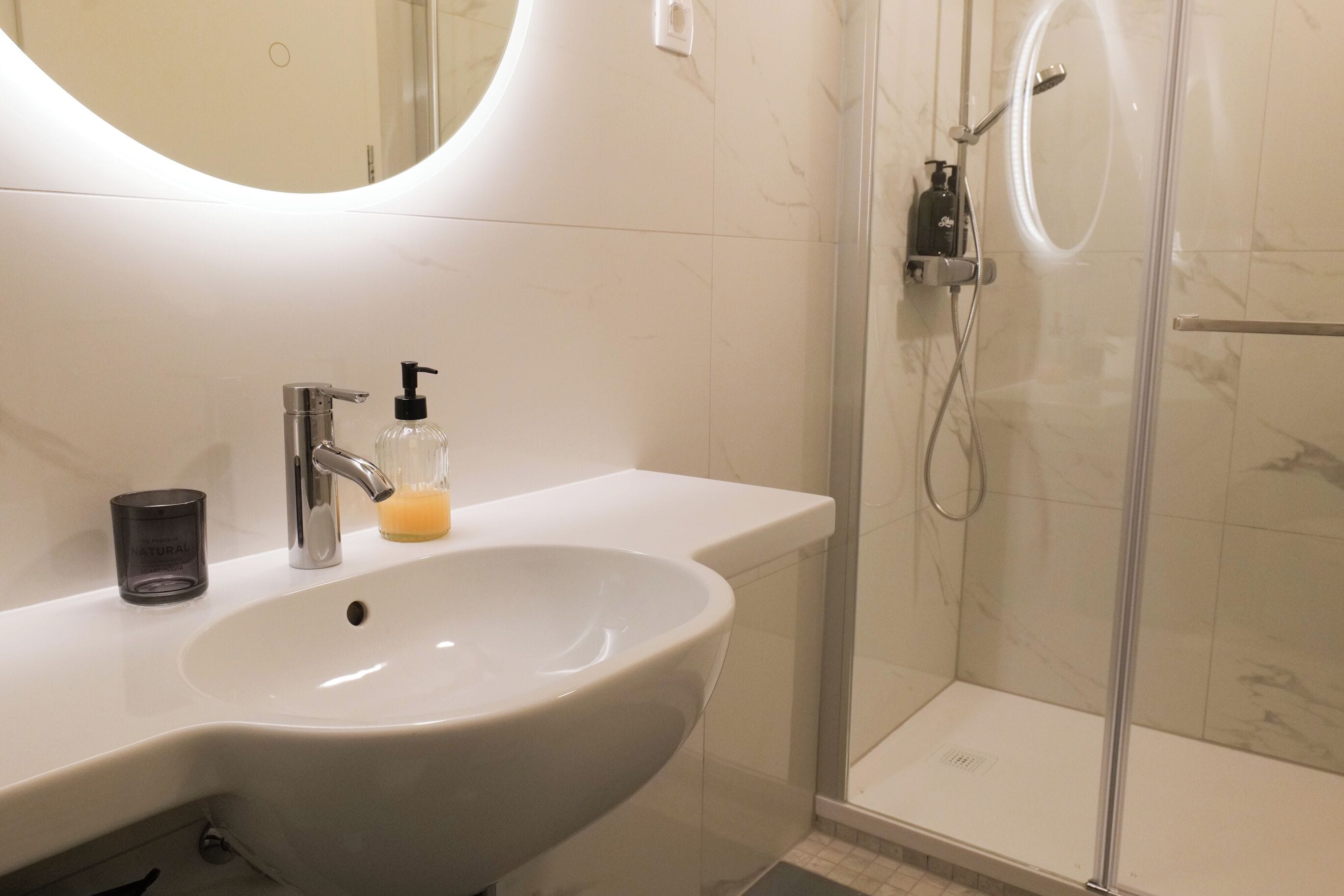 A bathroom with a large sink, a mirror, a shower, and a soap dispenser.