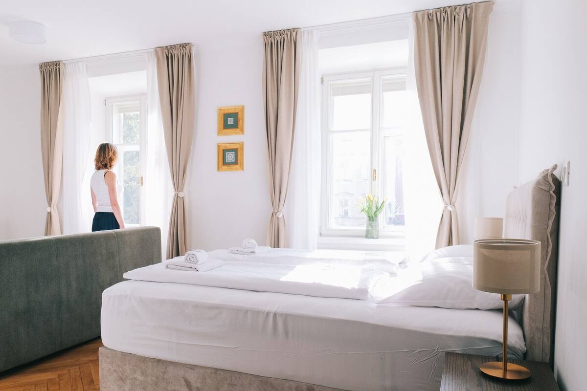 Una habitación de hotel con una cama, una lámpara de noche y un ventanal con cortinas.