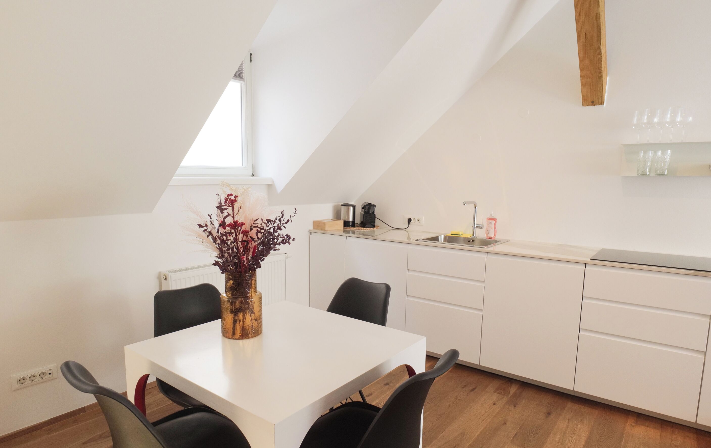 A modern kitchen with white cabinets, a white countertop, and a dining area with a white table and black chairs.