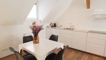 A modern kitchen with white cabinets, a white countertop, and a dining area with a white table and black chairs.