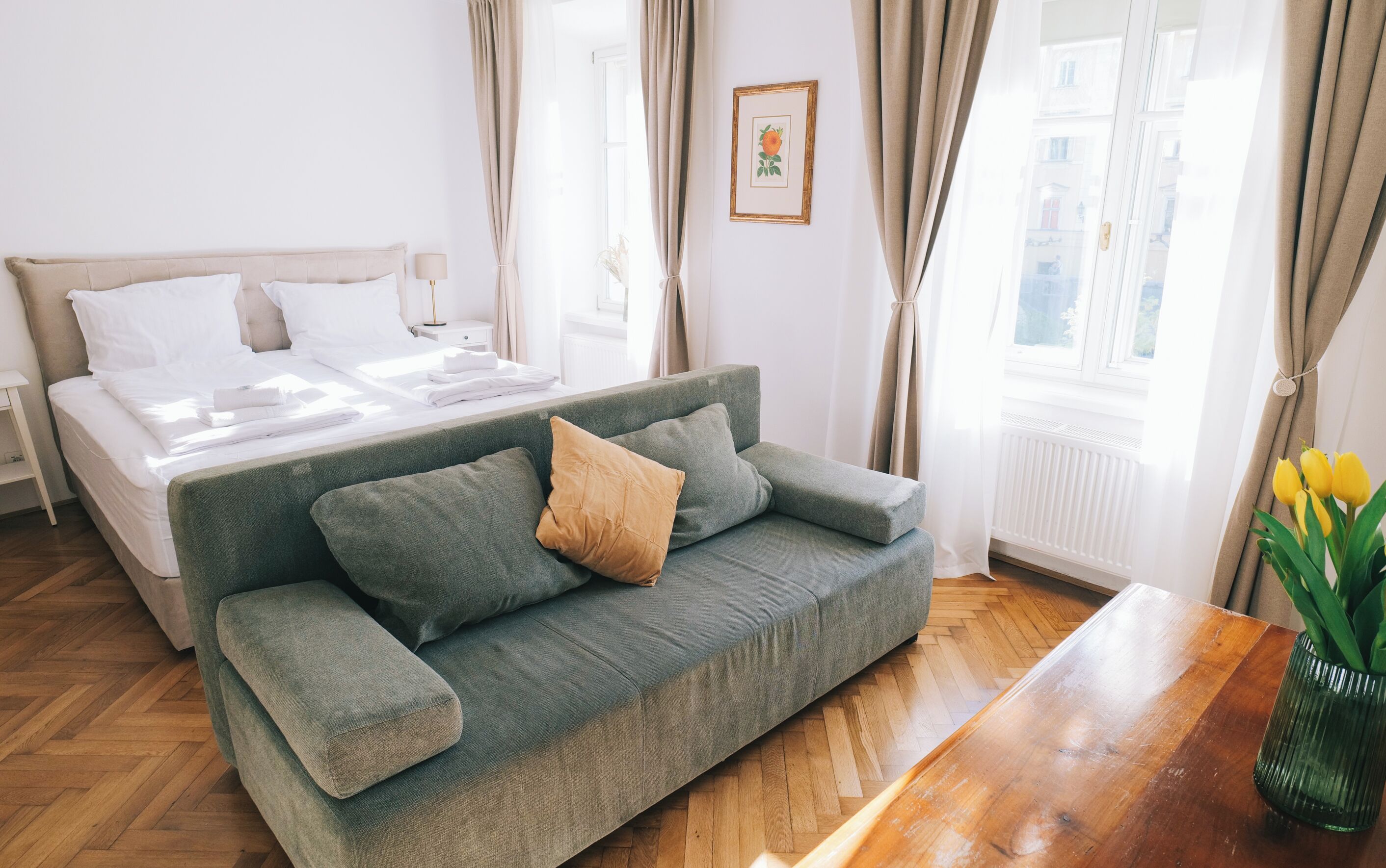 Ein modernes Hotelzimmer mit einem ordentlich bezogenen Bett, einem grünen Sofa und einem Holztisch.