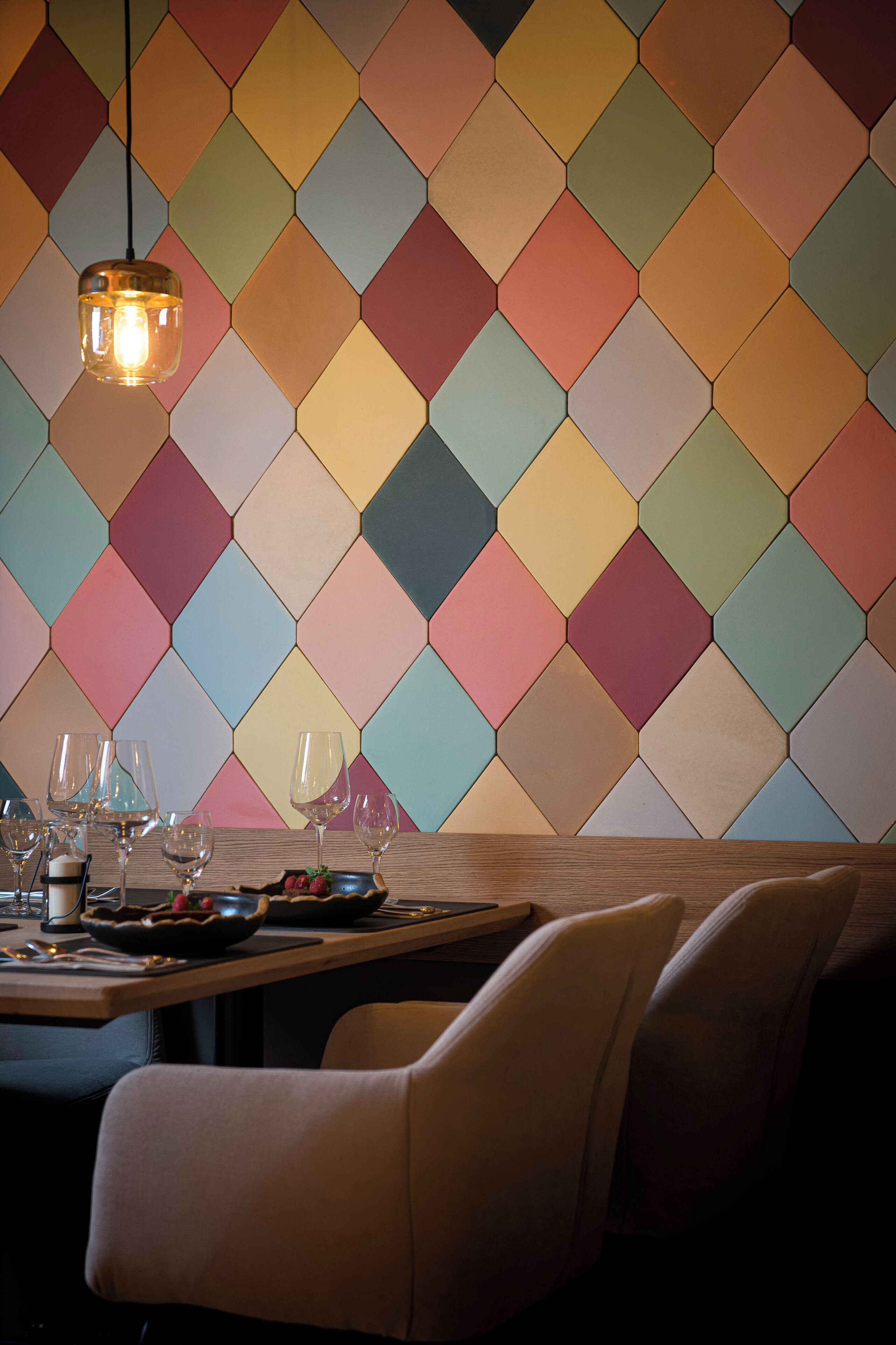 A dining area with a hexagonal patterned wall, a hanging light fixture, and a table set with glasses and plates.