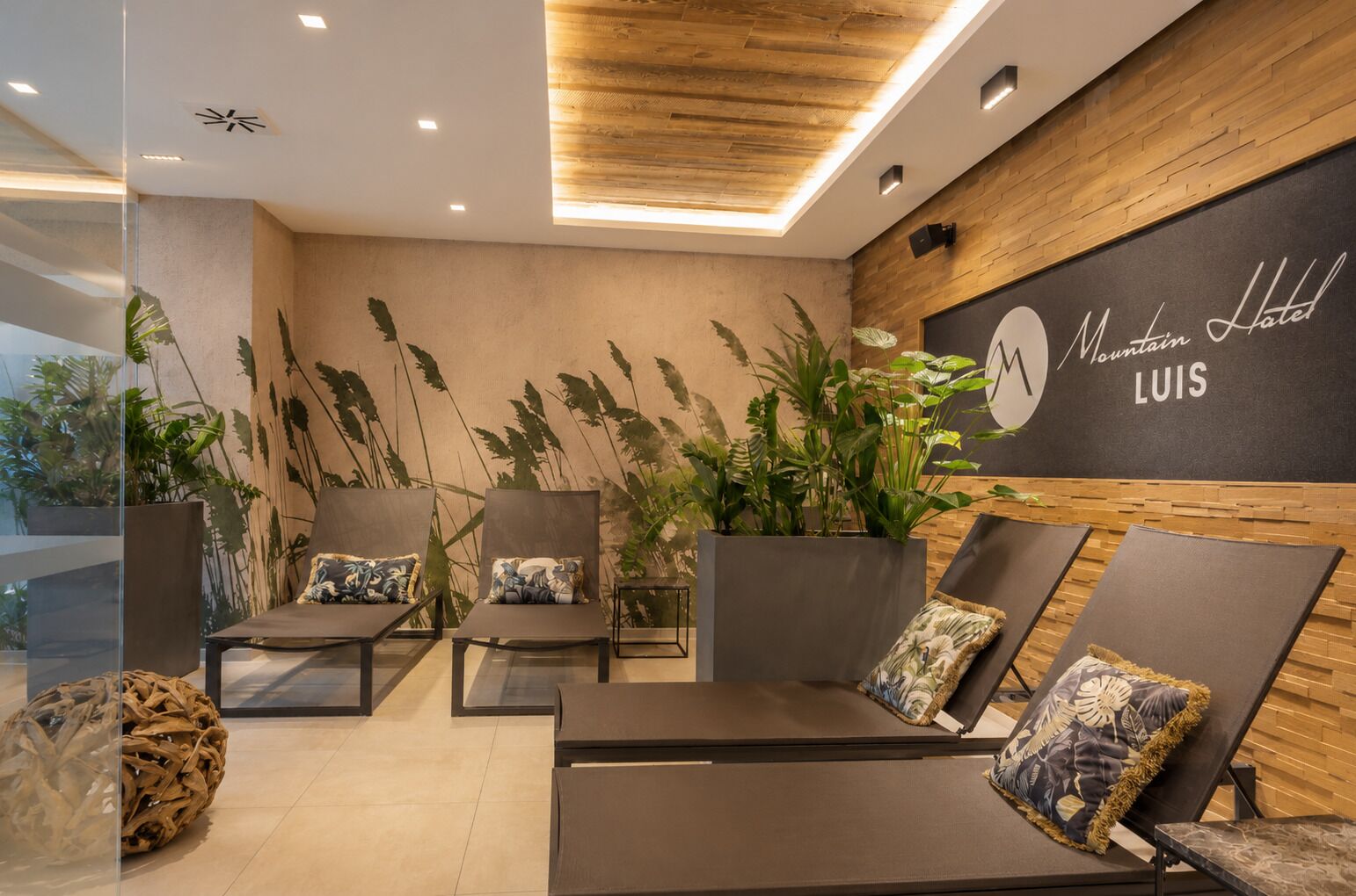 Un moderno vestíbulo de hotel con sillones, grandes macetas y un letrero en la pared que dice 'Mountain Hotel Luis'.