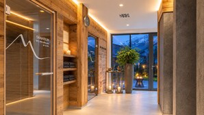 A modern spa with wooden walls, a visible clock, and a large window offering a view of the outside. - MOUNTAIN LUIS - HOTEL | SUITES | PENTHOUSES (Kaprun)