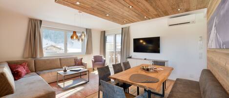 Una sala de estar moderna con techo de madera, un televisor grande, una mesa de comedor y un sofá.