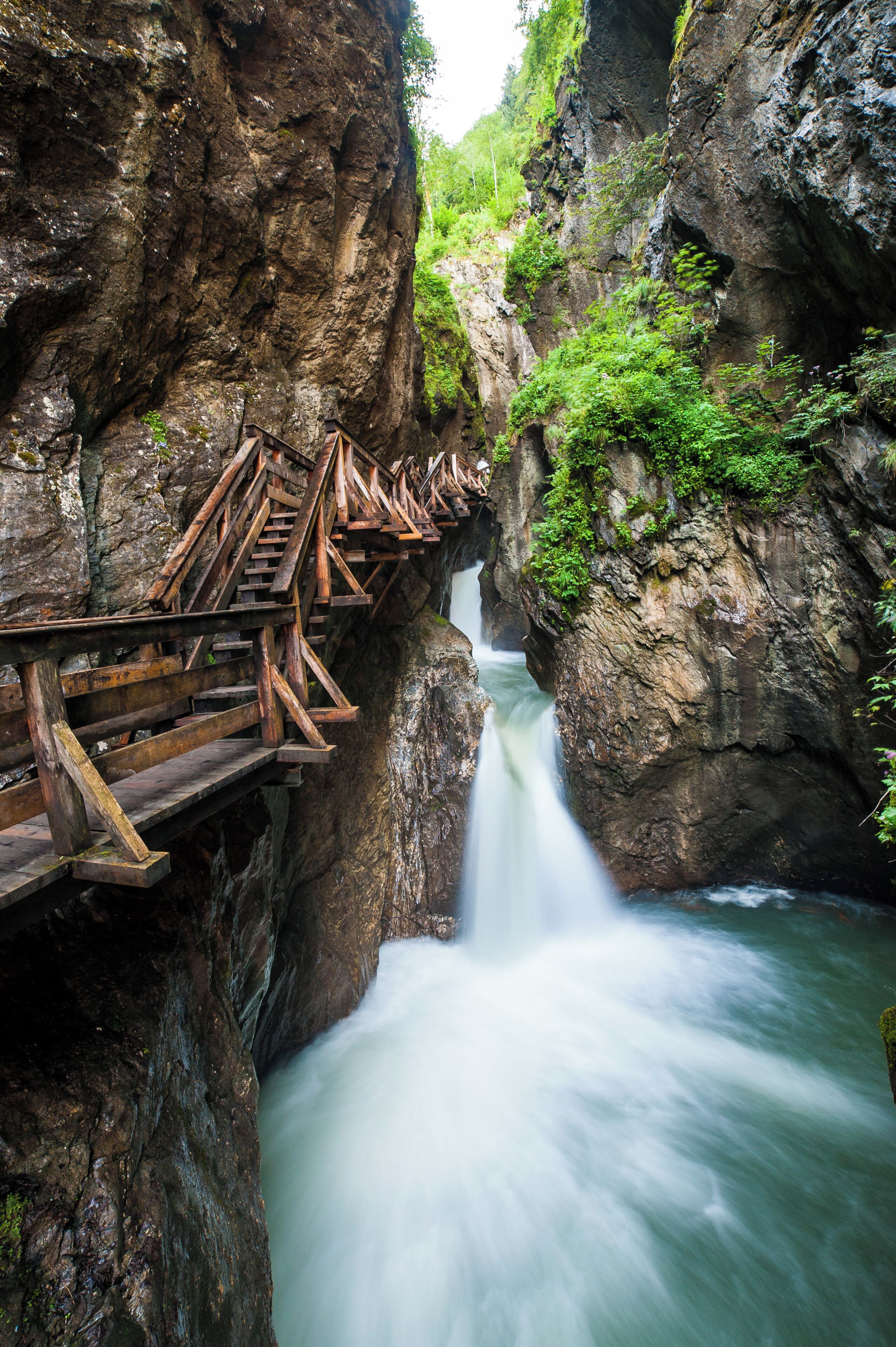 Un puente de madera cruza un río caudaloso en un desfiladero rocoso.