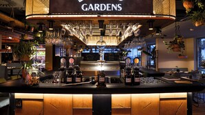 A bar area with a sign reading 'LUIS GARDENS,' glasses hanging above the bar, and a coffee machine in the background. - MOUNTAIN LUIS - HOTEL | SUITES | PENTHOUSES (Kaprun)
