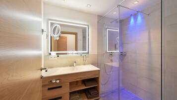 A modern bathroom with a wooden vanity, a glass shower enclosure, and a mirror with built-in lighting.