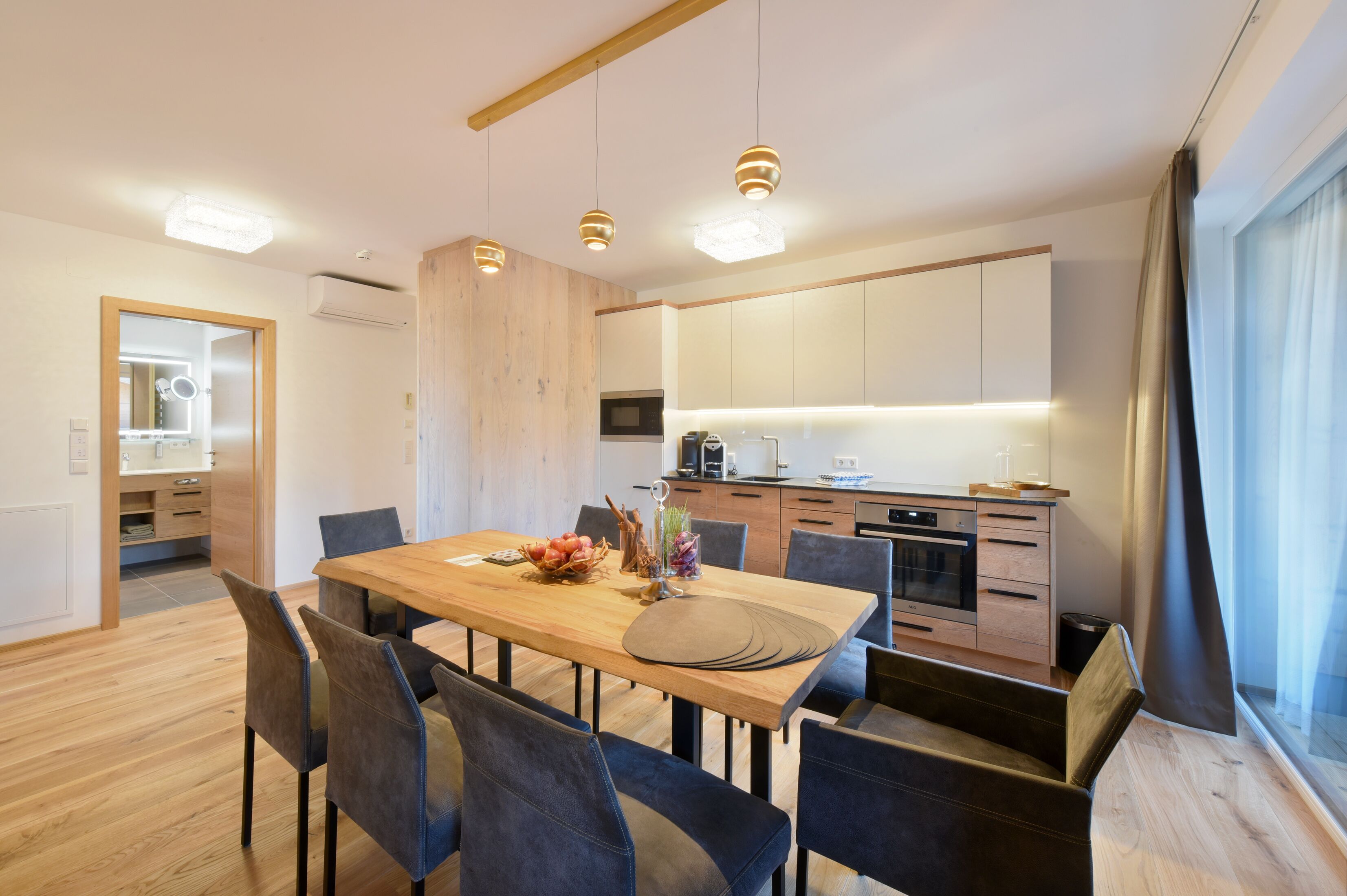 Une cuisine moderne avec des meubles en bois, une table à manger avec des chaises et des luminaires suspendus.