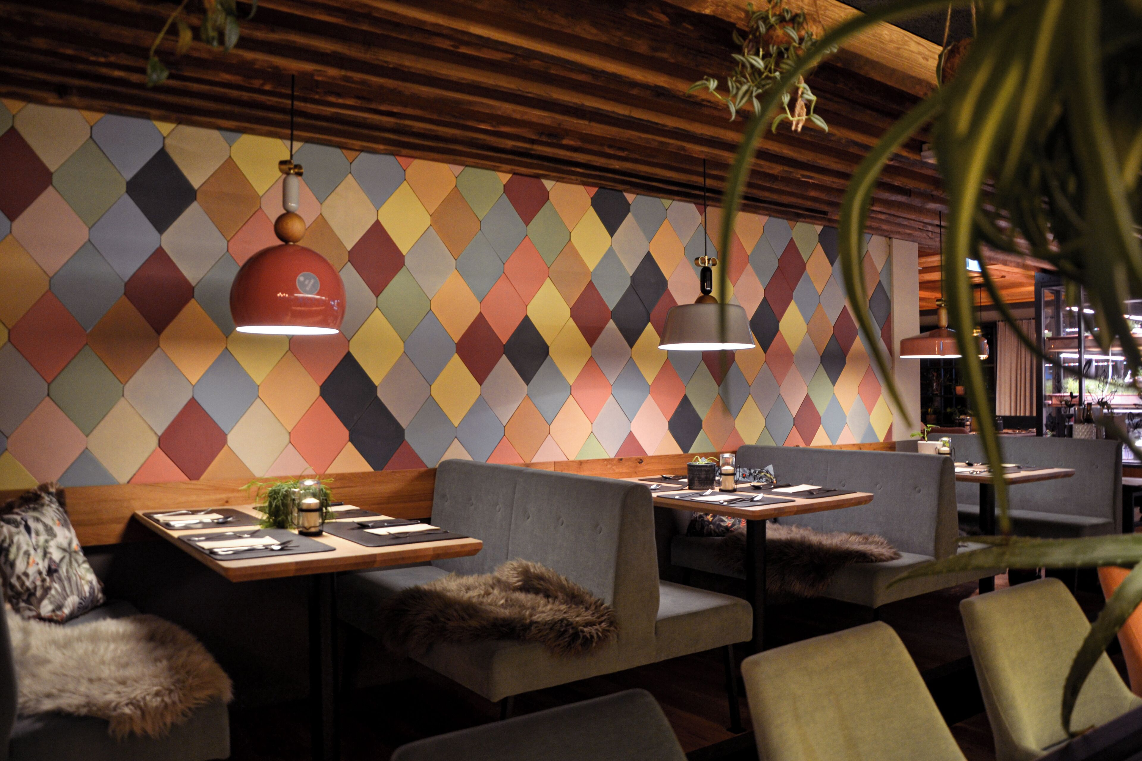 A restaurant interior with a geometric patterned wall, wooden ceiling, and modern seating.