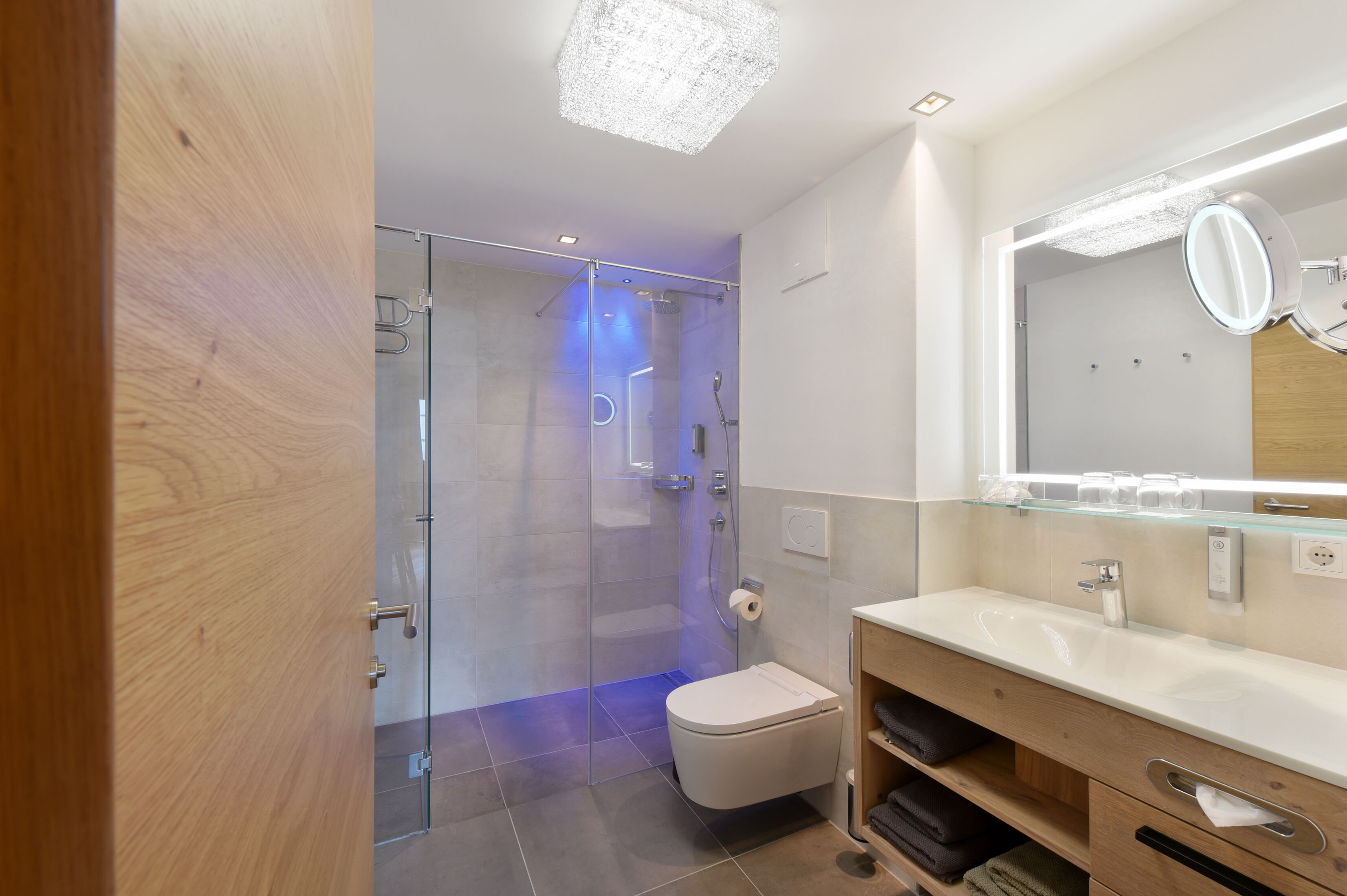 A modern bathroom with a glass shower enclosure, a white toilet, a vanity with a mirror, and a wooden cabinet.