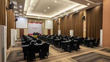 Un salón de conferencias con varias mesas y sillas, un atril y una pantalla que muestra "RAMADA".
