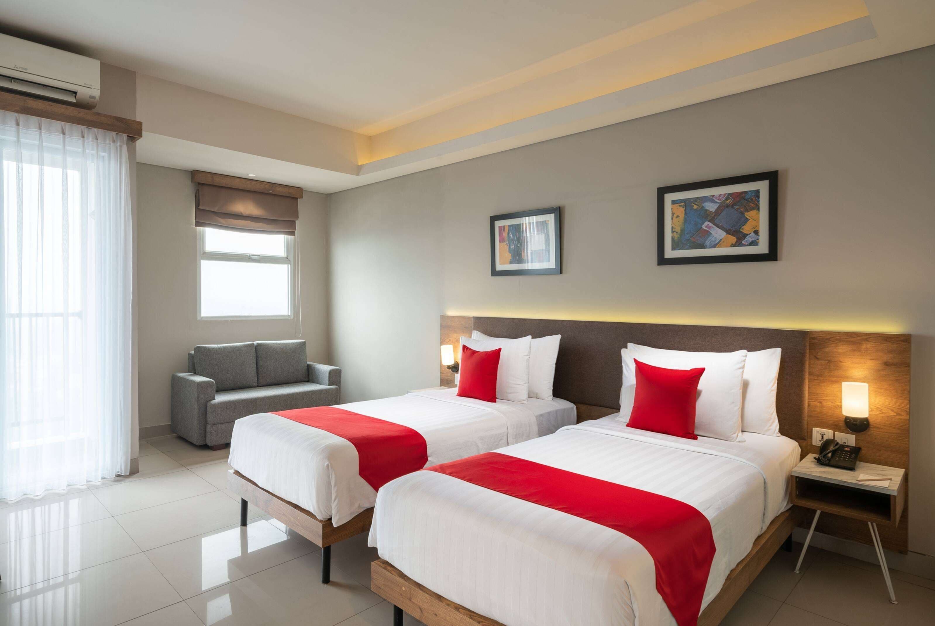 Une chambre d’hôtel avec deux lits, un canapé, une petite table et une table de chevet avec une lampe.