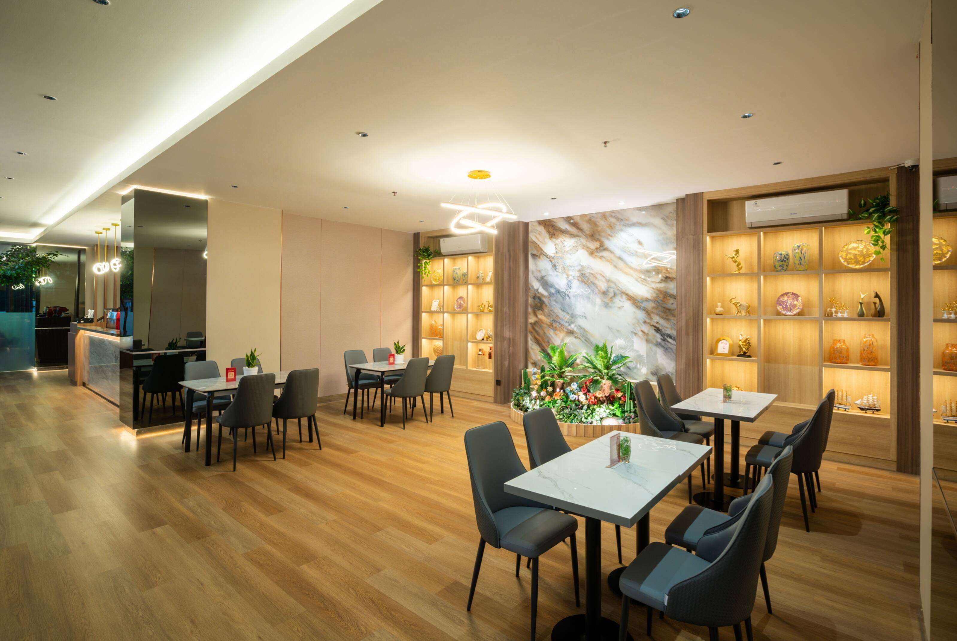 A modern dining area with wooden flooring, marble-topped tables, and black chairs. There are shelves with decorative items and a large wall mural.