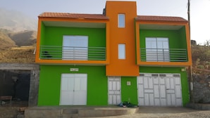 A two-story building with green and orange exterior walls, white doors, and a balcony. - Casa Tchichi (São Filipe)