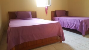 Two single beds with wooden headboards and a window above them. - Casa Tchichi (São Filipe)