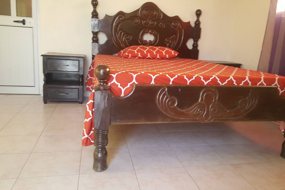 Uma cama com colcha estampada, cabeceira de madeira e mesa de cabeceira com gavetas.