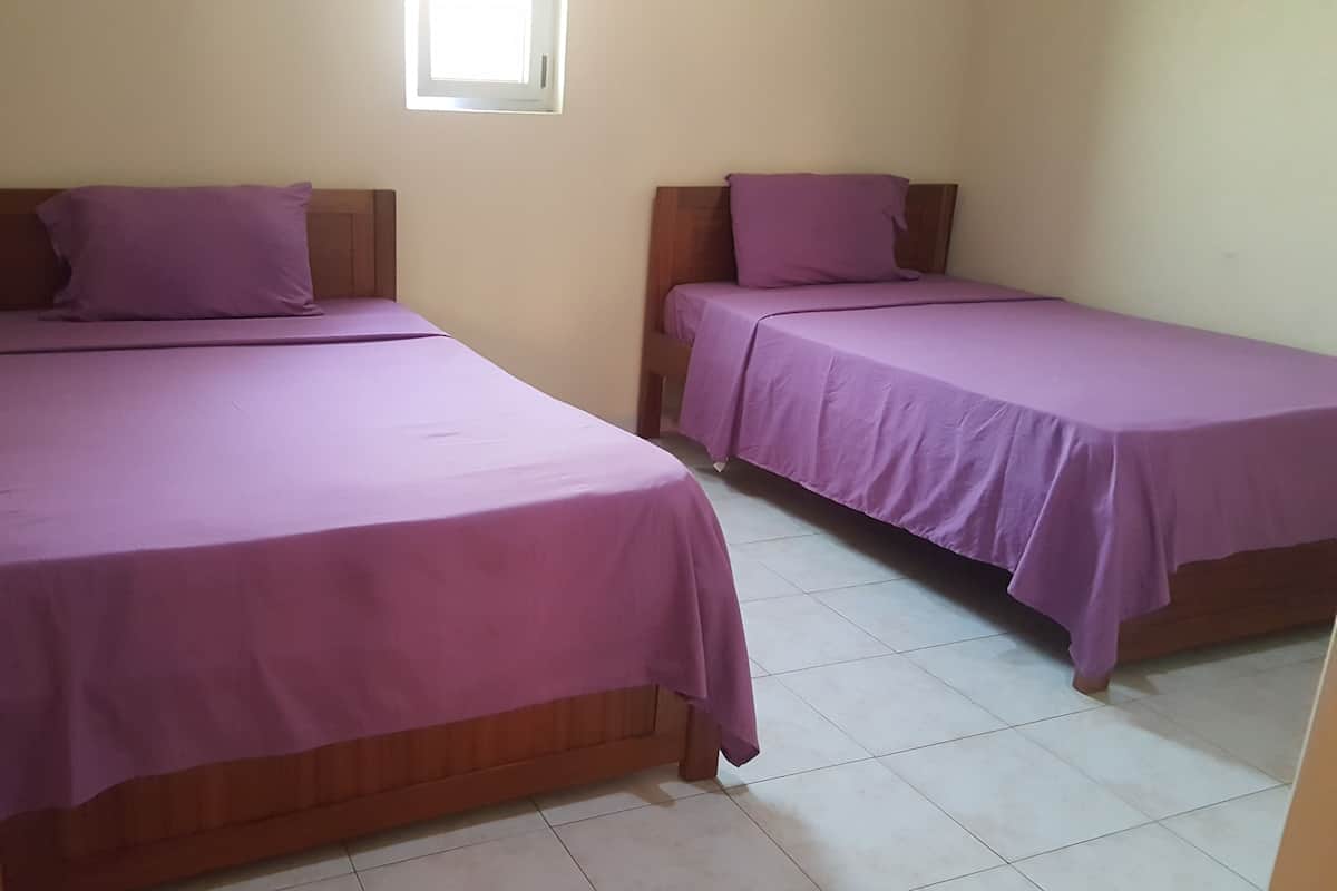 Duas camas de solteiro com cabeceiras de madeira e roupa de cama roxa em um quarto com piso de azulejos.